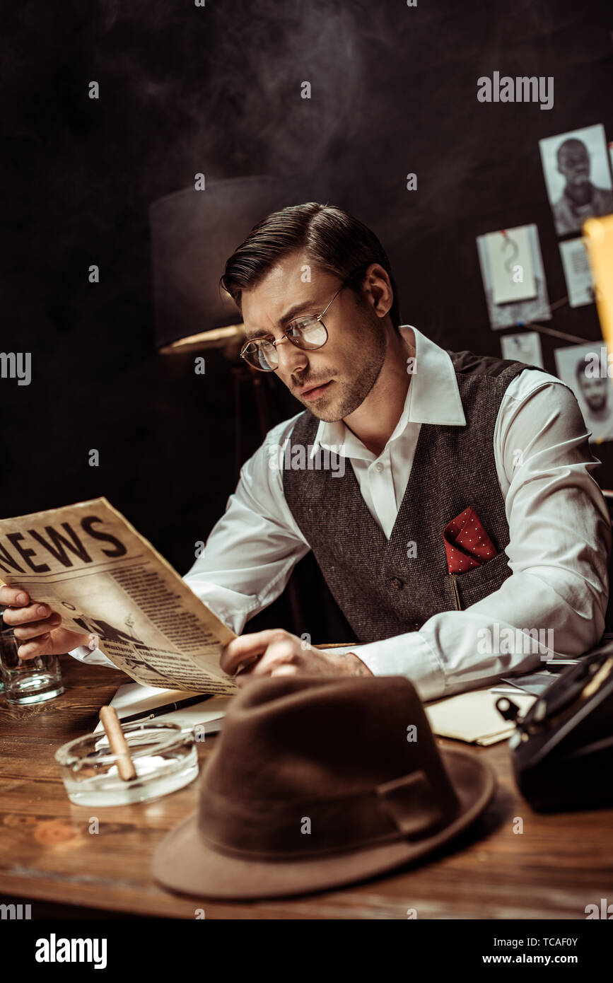 Concentrated detective in glasses reading newspaper in dark office