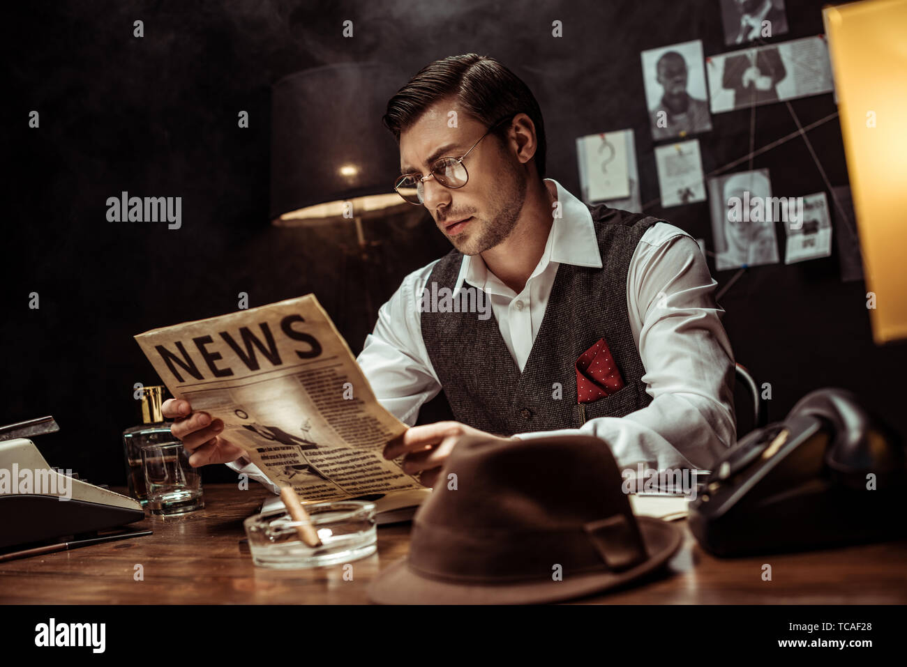 Concentrated detective in glasses reading newspaper in dark office