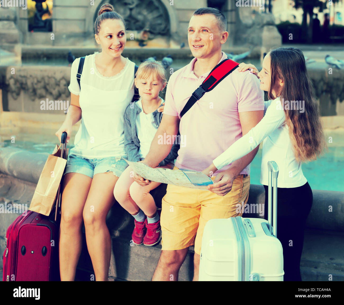 Cheerful family of four with suitcases - Cheerful Family Of Four With Suitcases Visiting Sights Of European City With Map TCAH4A 
