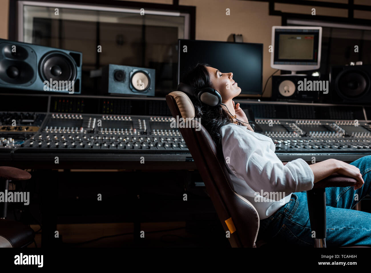 pretty sound producer listening music in headphones while sitting in office chair in recording studio Stock Photo