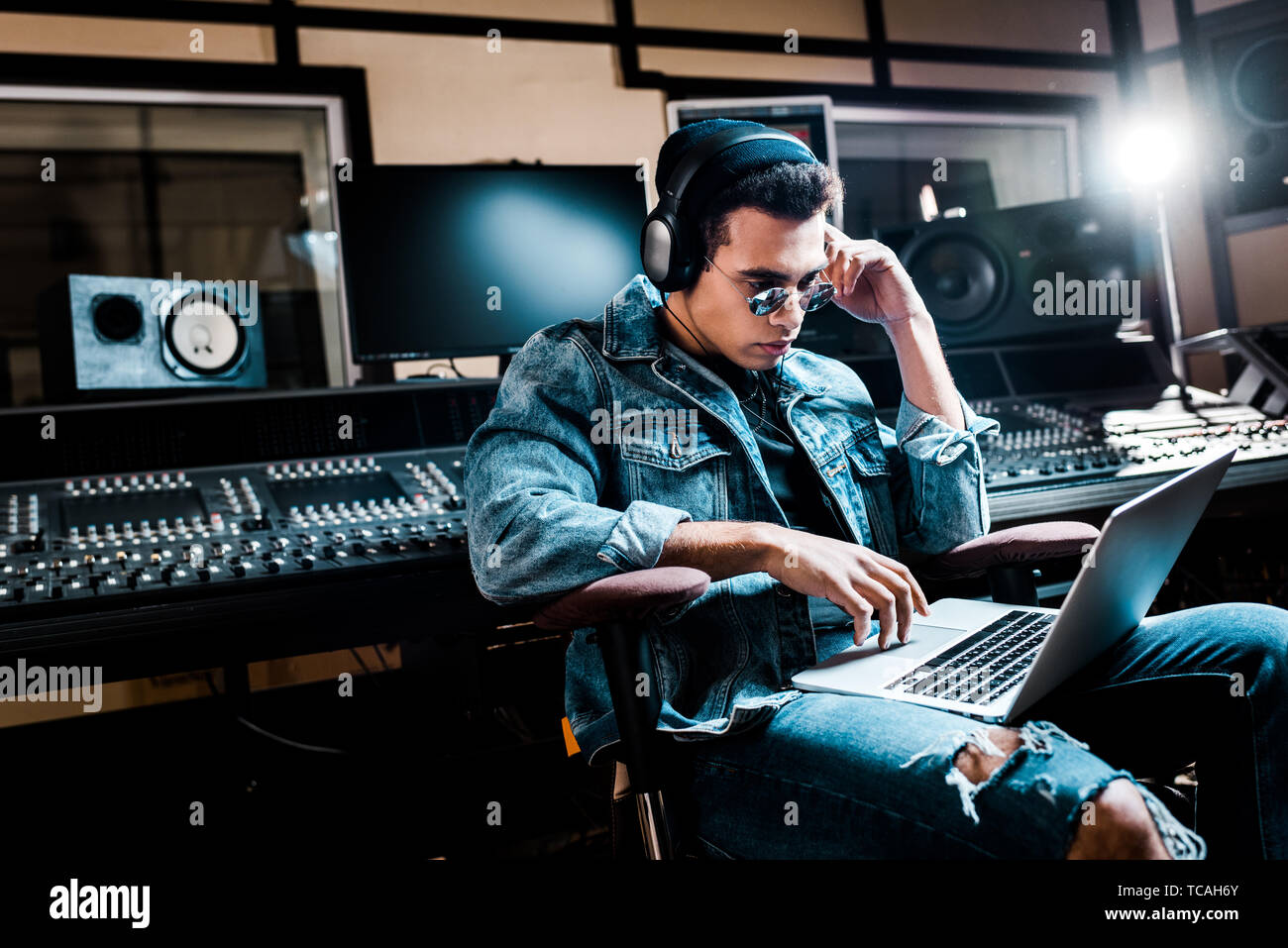 concentrated mixed race sound producer in headphones using laptop in recording studio Stock Photo