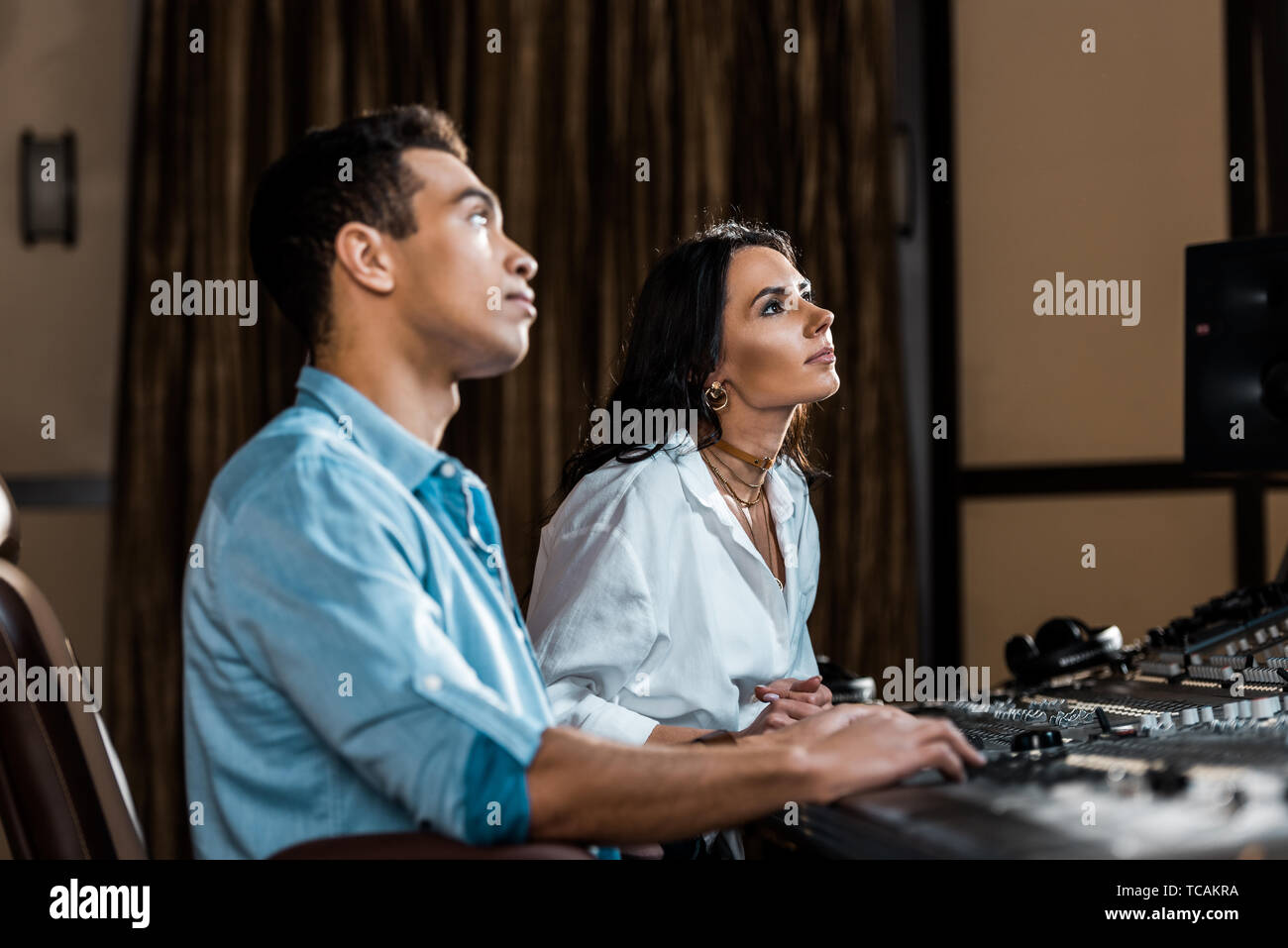 two attentive multicultural colleagues working at mixing console in recording studio Stock Photo