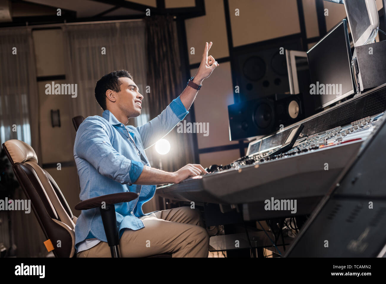 handsome mixed race sound producer showing victory sign while working in recording studio Stock Photo