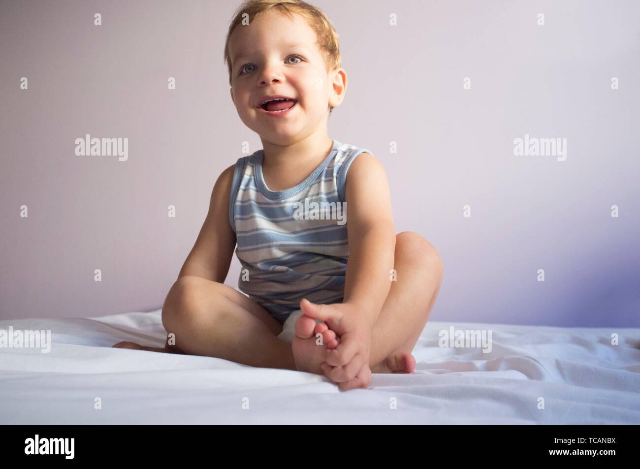 Very happy 2 years boy sitting on bed. Positive feeling at home. Soft noise at 100%. Stock Photo