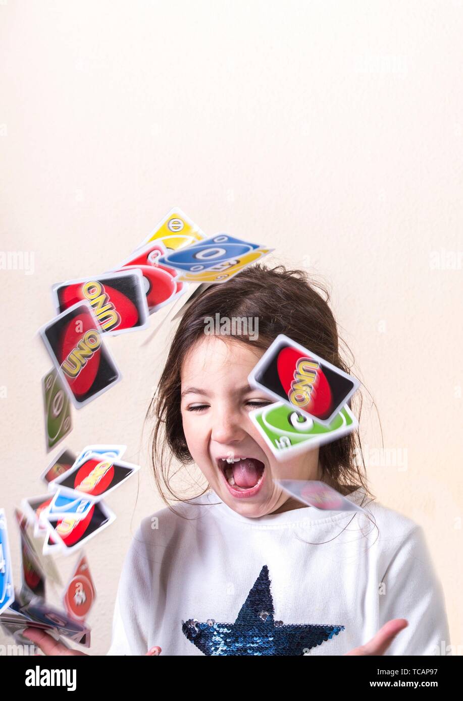 Little girl playing with UNO cards. She is launching into the air the cards. Stock Photo