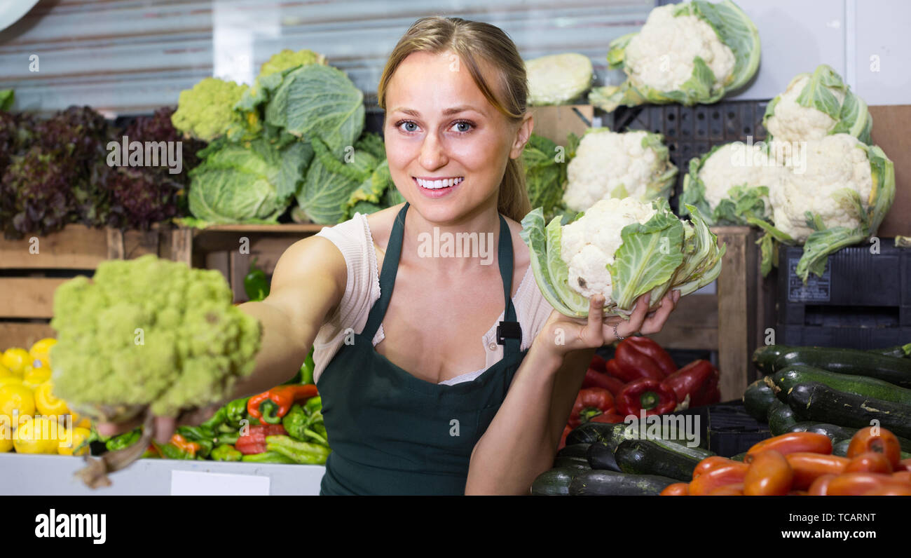 glad young woman in apron showing fresh cabbage on marketplace Stock ...