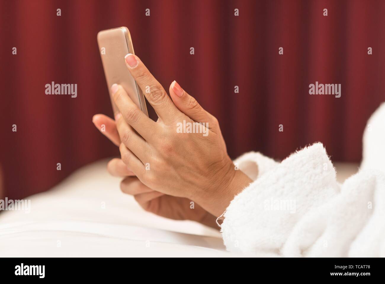 Young woman in bathrobe lying in hotel room using mobile phone, relaxed