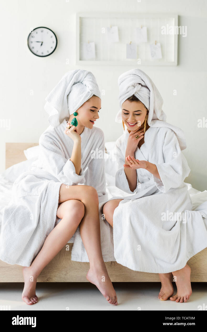 https://c8.alamy.com/comp/TCATXM/stylish-smiling-girls-in-earrings-bathrobes-and-with-towels-on-heads-talking-while-sitting-on-bed-TCATXM.jpg