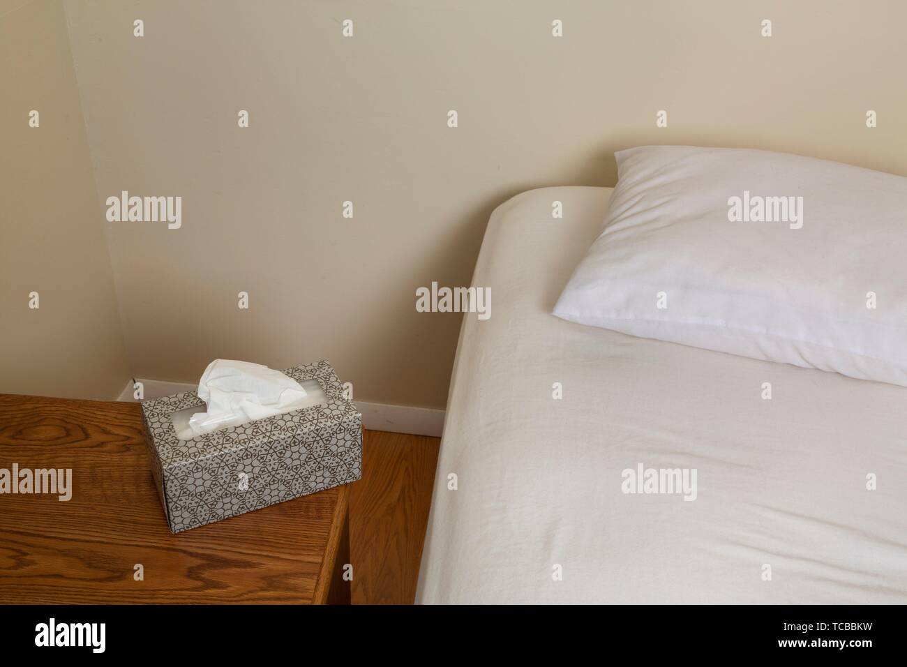 Empty unmade bed and a night table with a box of facial tissues on it. Stock Photo
