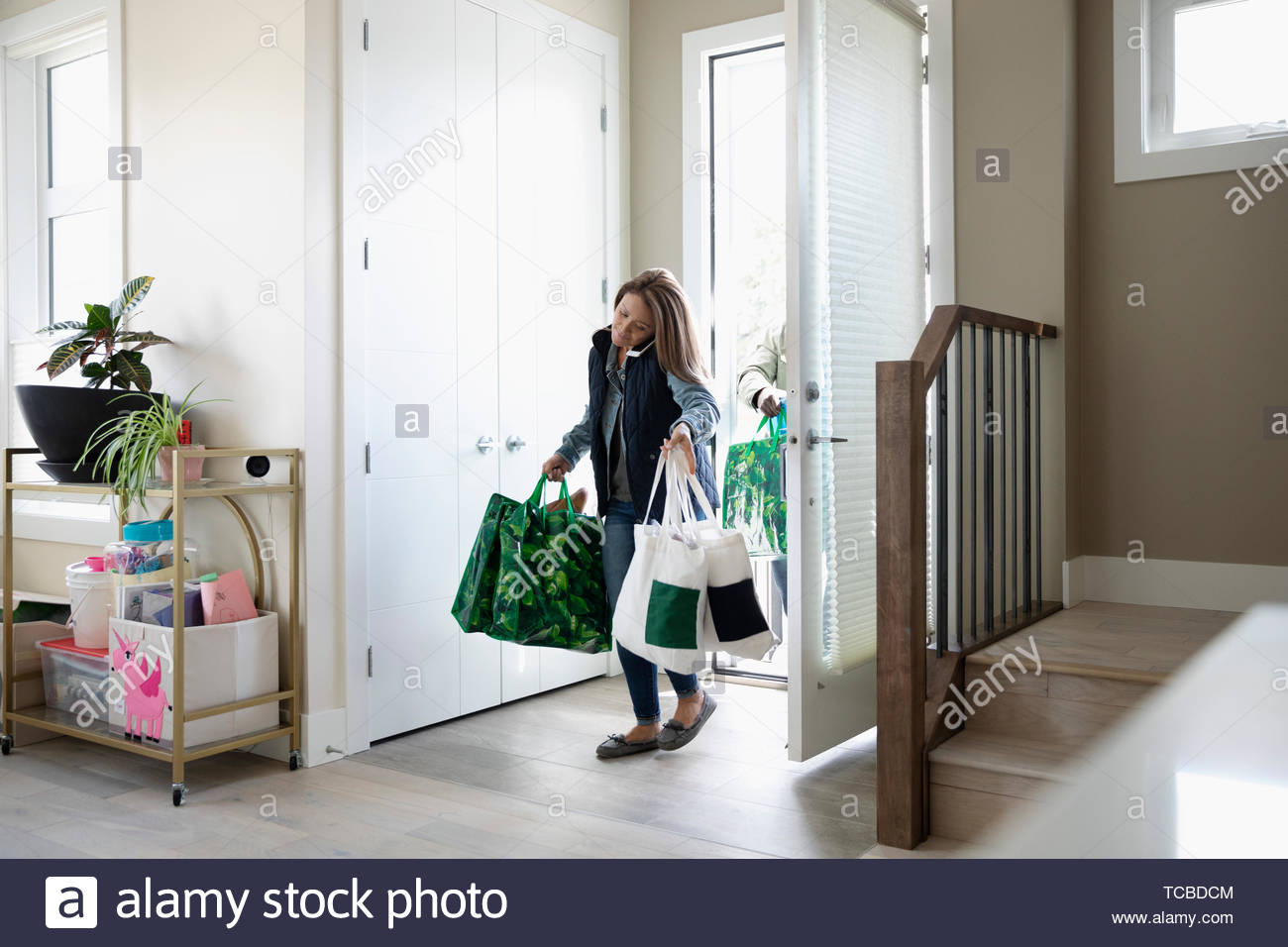 Woman with groceries talking on smart phone, entering house Stock Photo