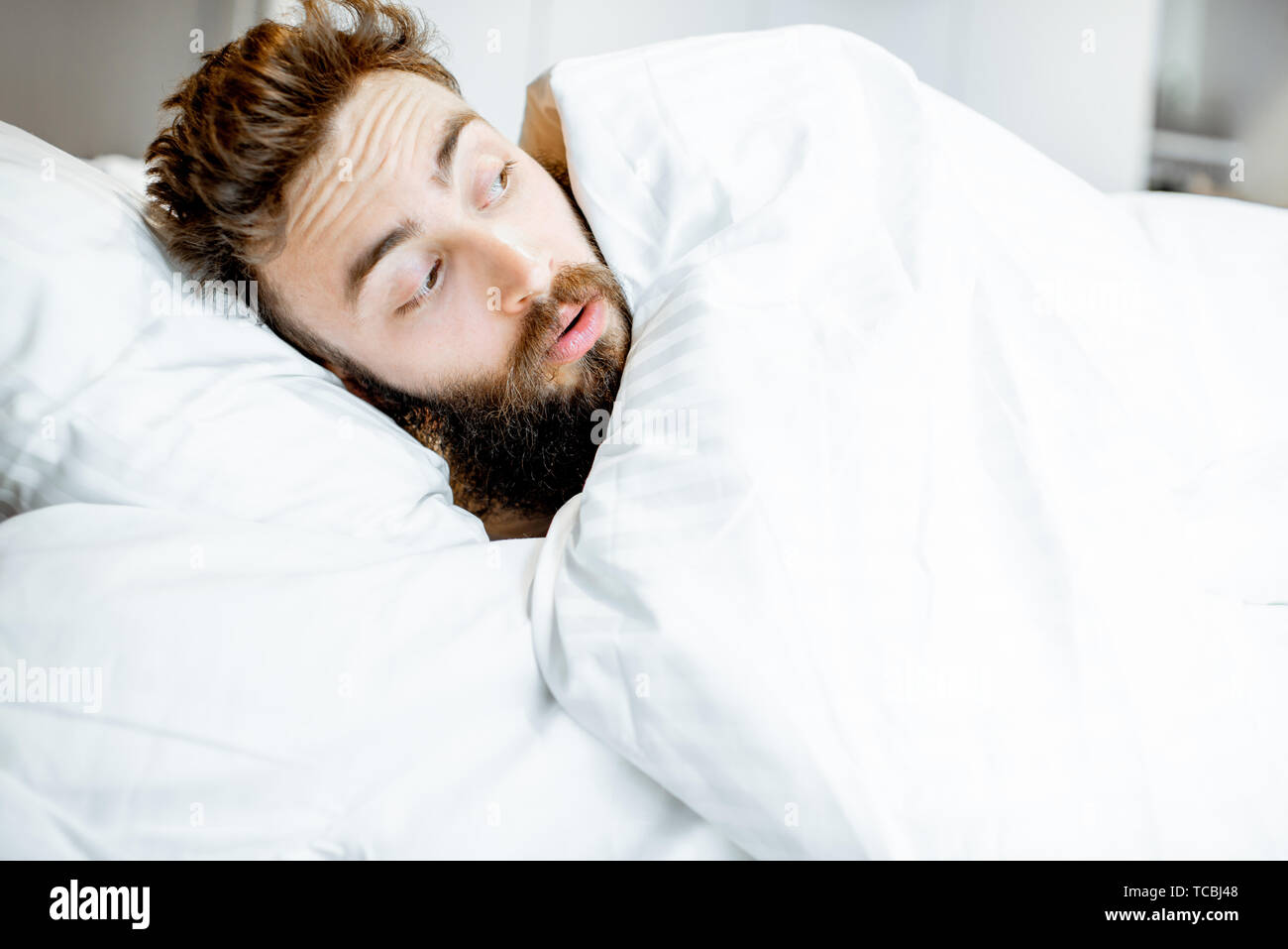 Man hiding in bed under the white sheets feeling scared alone Stock Photo
