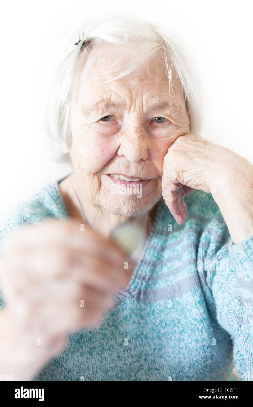 Cheerful elderly 96 years old woman sitting at table at home happy with a coin in her hand. Saving for retirement and financial planing concept Stock Photo