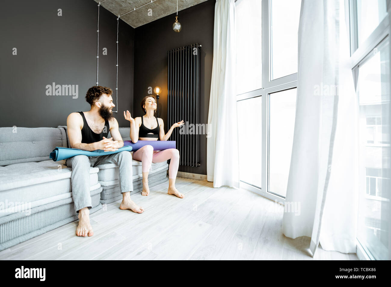 Young Couple In Sportswear With Yoga Mats Talking Together After