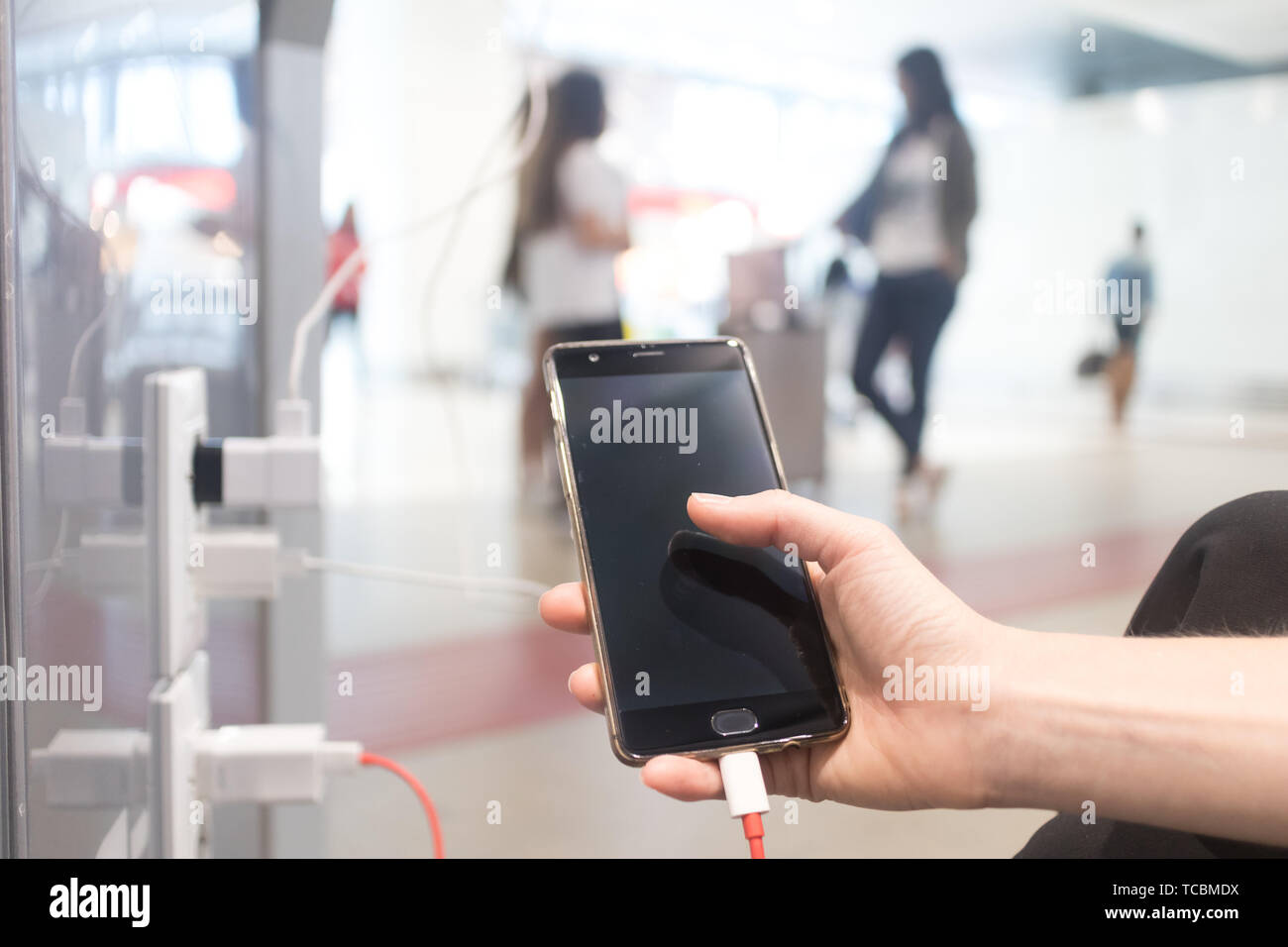 Female hands holding and using smartphone while charging it in a public