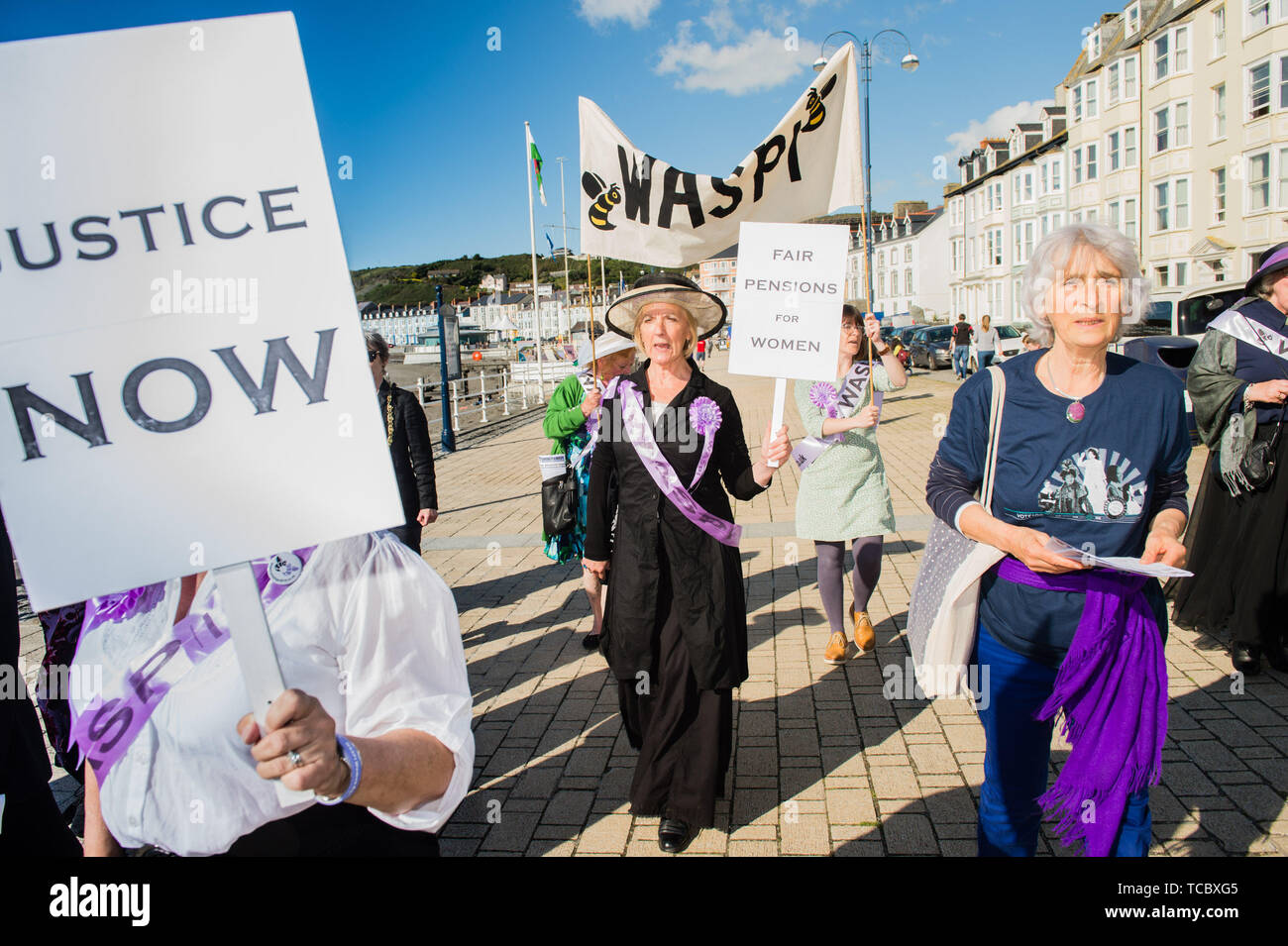 Aberystwyth Wales UK, Thursday 06 June 2019  A group of placard-carrying grannies in their 60s, dressed as suffragettes  marching along the promenade in Aberystwyth as part of a nation-wide protest against the raising of the state pension age for women . WASPI [Women Against State Pension Injustice] are campaigning to reverse the decision to change  the pension age to 67  for women born in the 1950’s . There are 5,000 women in Ceredigion born in the 1950s who have lost years of their pensions as a result of the Government’s acceleration policy. The legality of these changes is now being tested Stock Photo