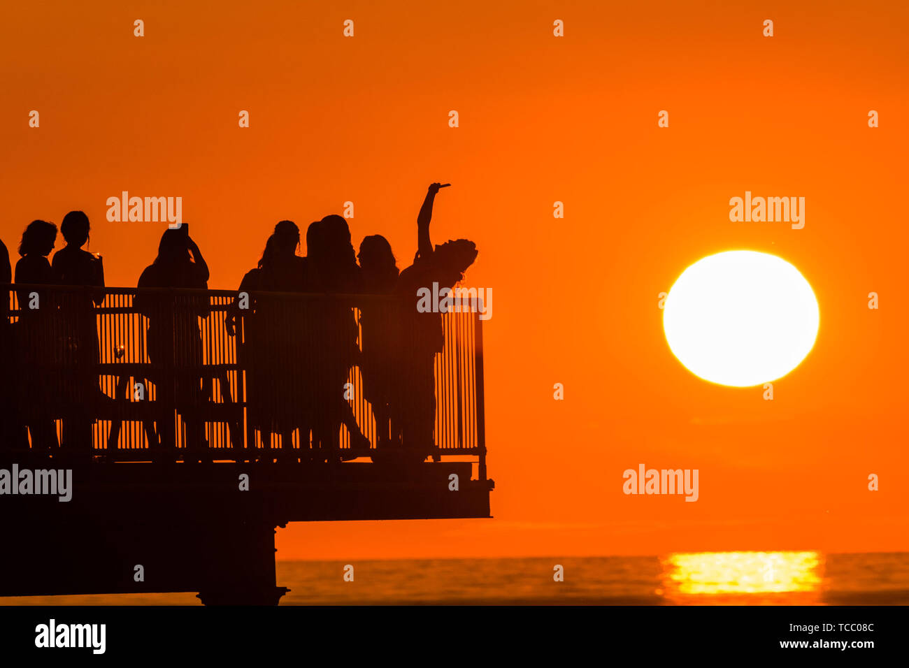 Aberystwyth Wales UK, Thursday 06 June 2019  A glorious orange sunset behind a grouf of students celebrating the end of term on a  warm and clear summer evening in Aberystwyth on the west wales coast, at the end of a day of intense rain showers and bright sunshine  photo credit Keith Morris / Alamy Live News Stock Photo