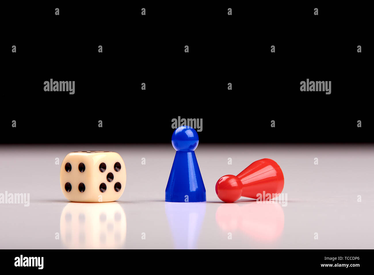 Standing blue playing figurine as winner and lying red figurine as loser with playing dice on white table top with black background. Space for your te Stock Photo