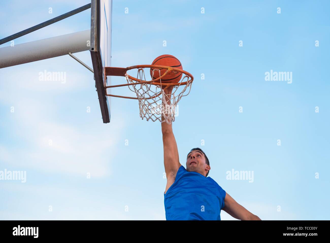 Street basketball athlete performing slam dunk on the court. Stock Photo