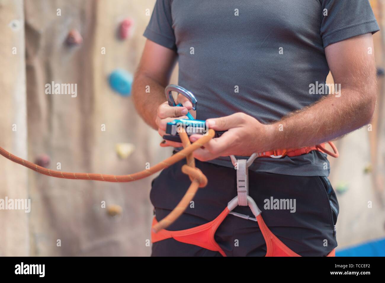 Rock wall climber wearing safety harness and climbing equipment indoor
