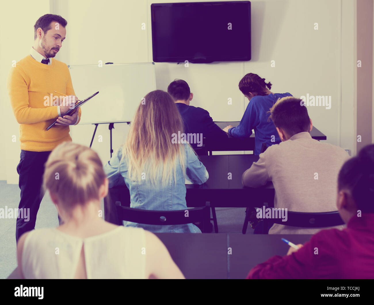 Adult male teacher inspecting working process of students during exam in class Stock Photo