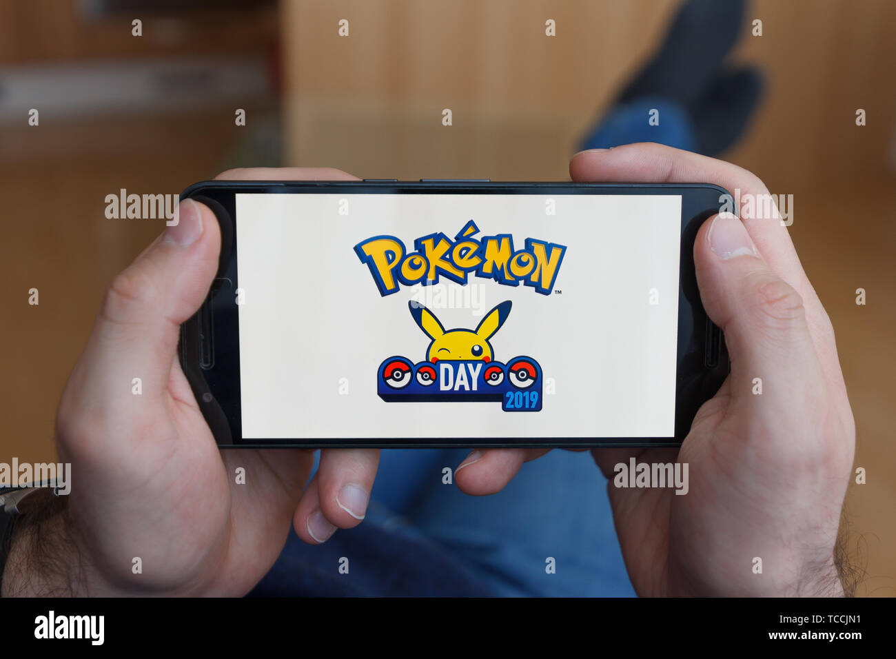 LOS ANGELES, CALIFORNIA - JUNE 3, 2019: Lying Man holding a smartphone and playing the Pokemon Go game on the smartphone screen. An illustrative edito Stock Photo