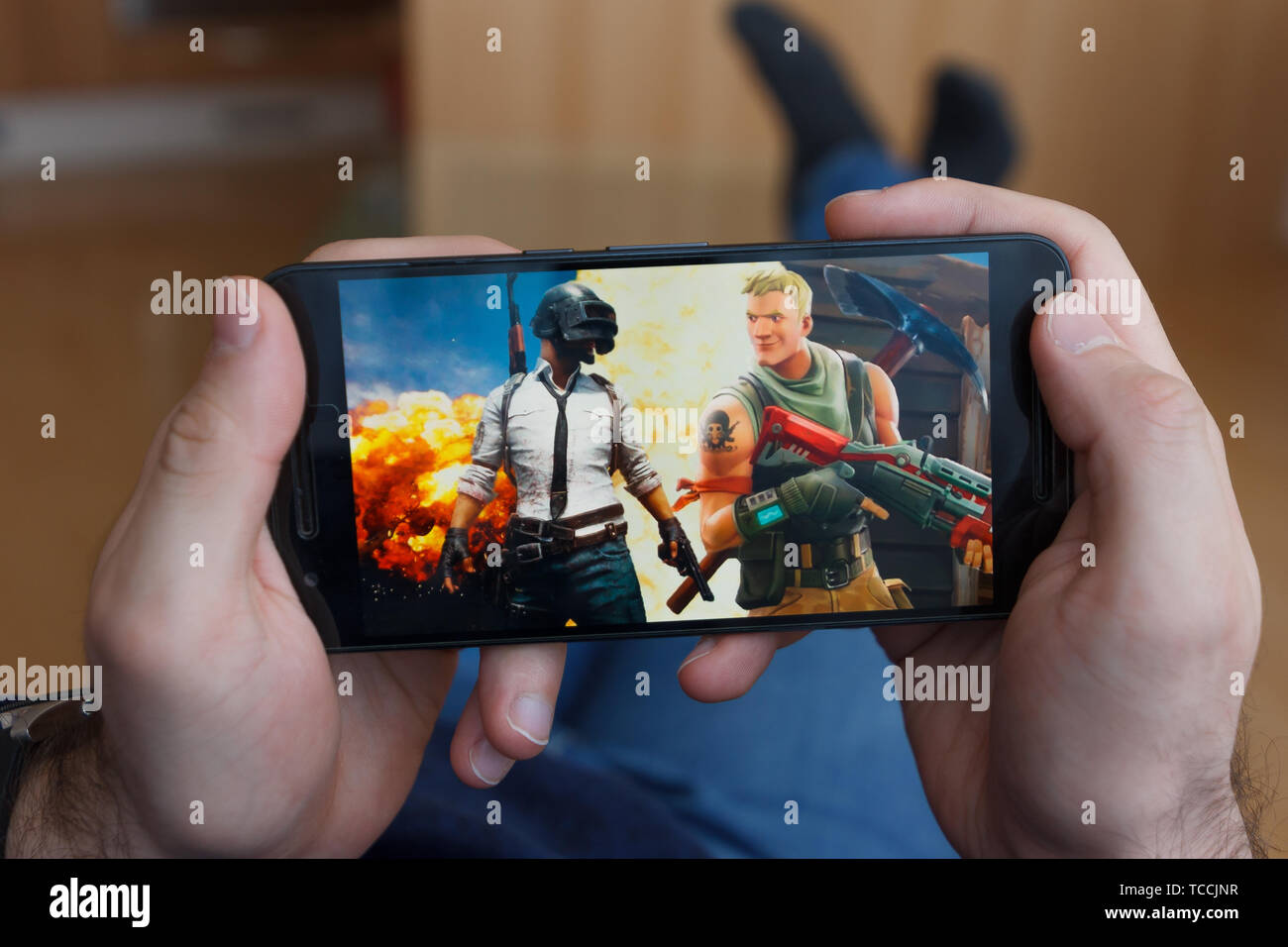 LOS ANGELES, CALIFORNIA - JUNE 3, 2019: Lying Man holding a smartphone and compares PUBG and Fortnite games on the smartphone screen. An illustrative  Stock Photo