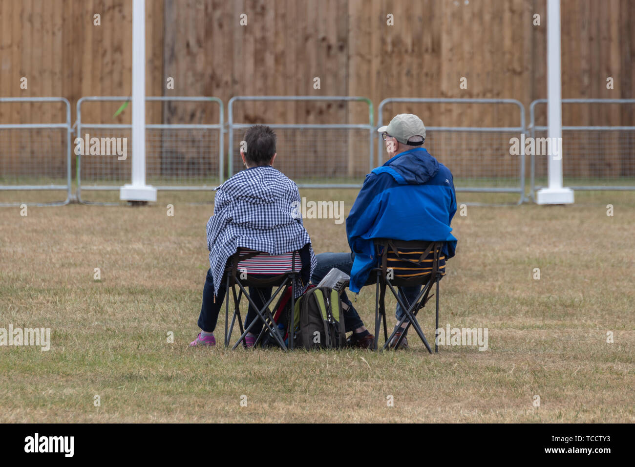 an elderly couple sat on fold chairs or camping chairs at an outdoor