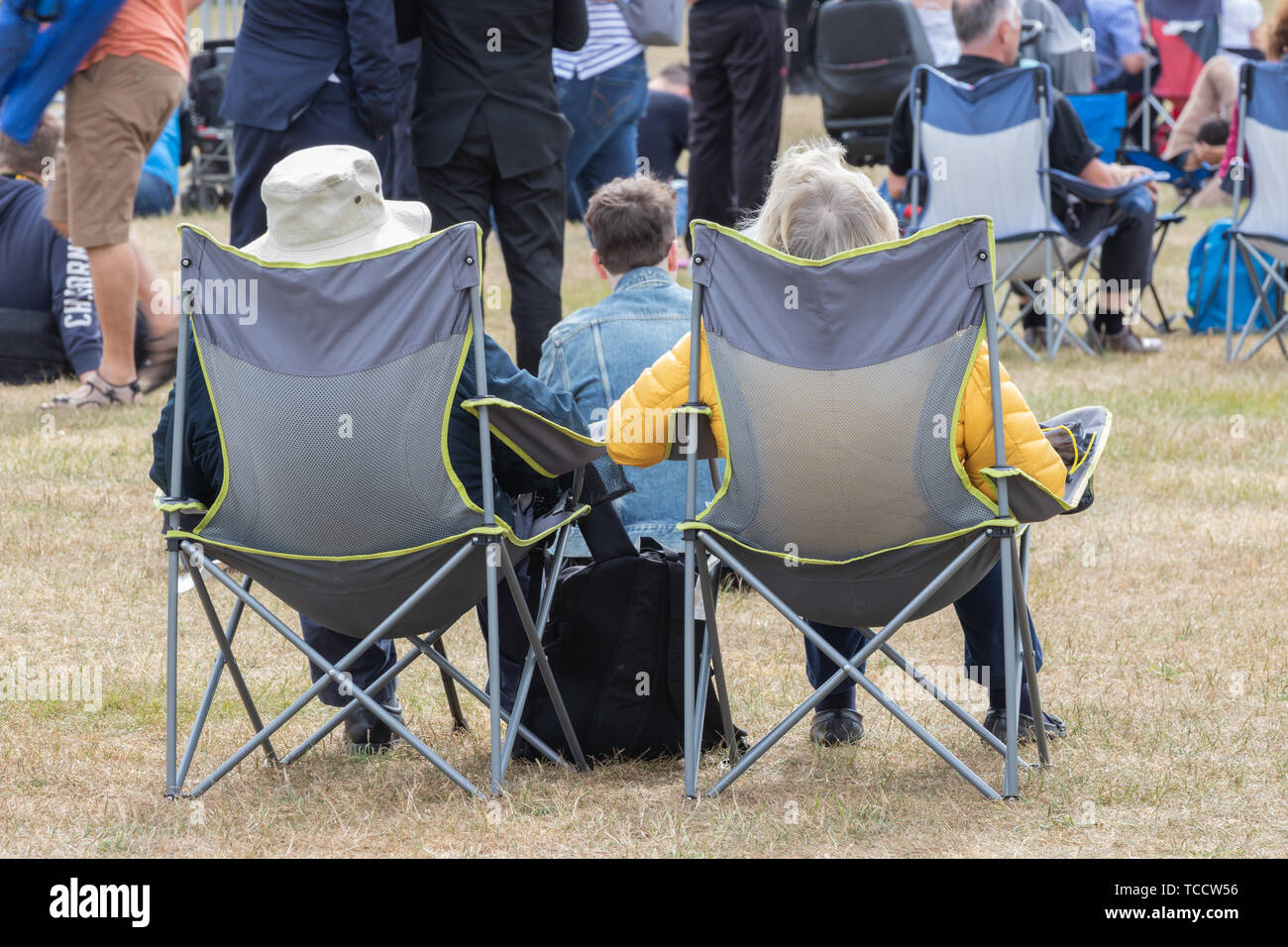 an elderly couple sat on fold chairs or camping chairs at an outdoor