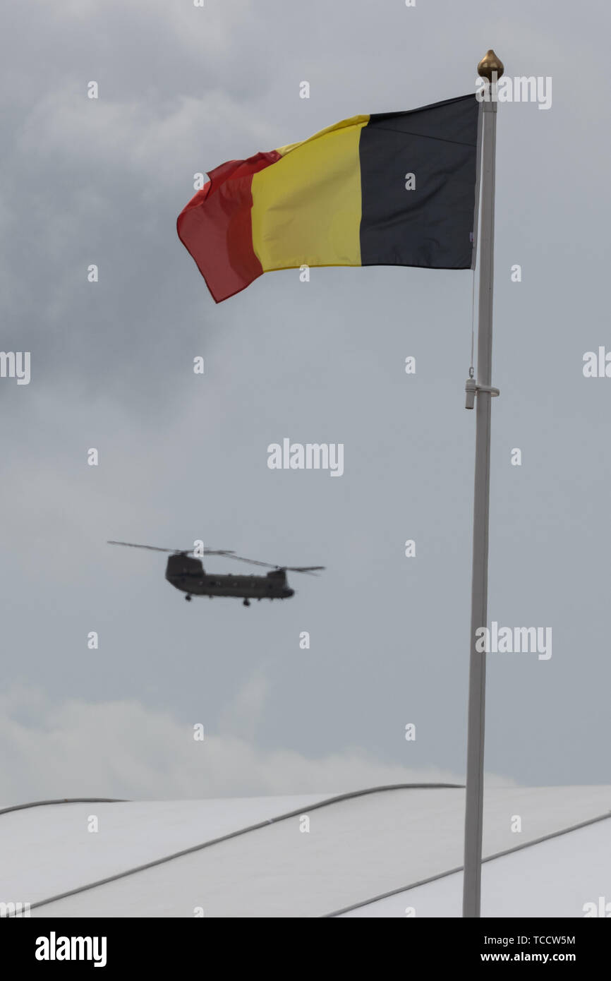 A chinnook helicopter flying past a Belgian flag on a flag pole Stock Photo