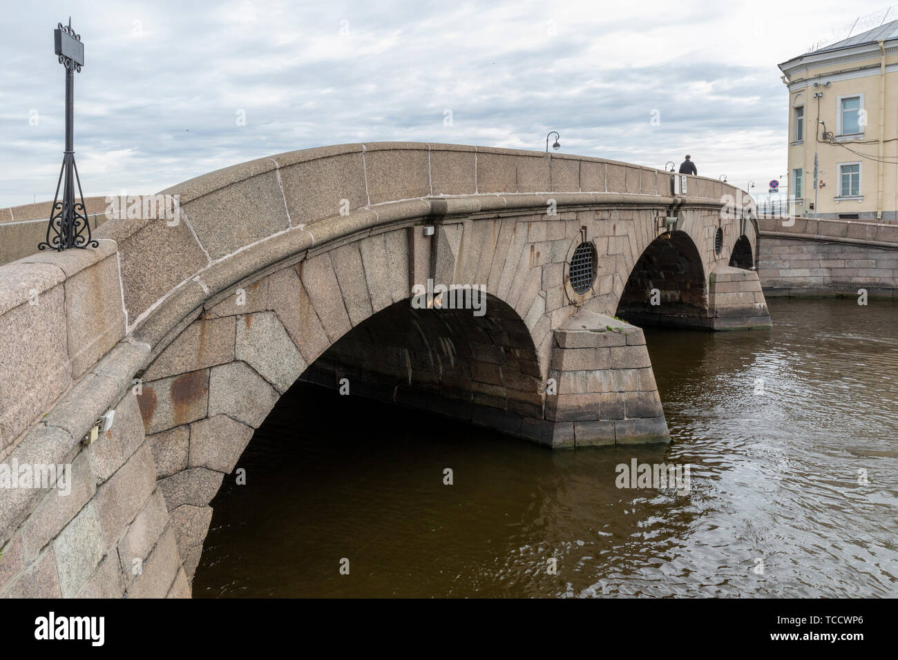 Lone pedestrian crossing stone arch bridge over Fontanka River at Summer Garden that connects Palace & Kutuzov Embankments, St Petersburg, Russia Stock Photo