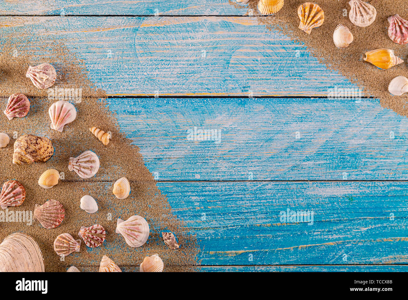 Summer time concept with sea shells on a blue wooden background and sand. Seashells frame on wooden background nautical border. Focus on seashells. Stock Photo