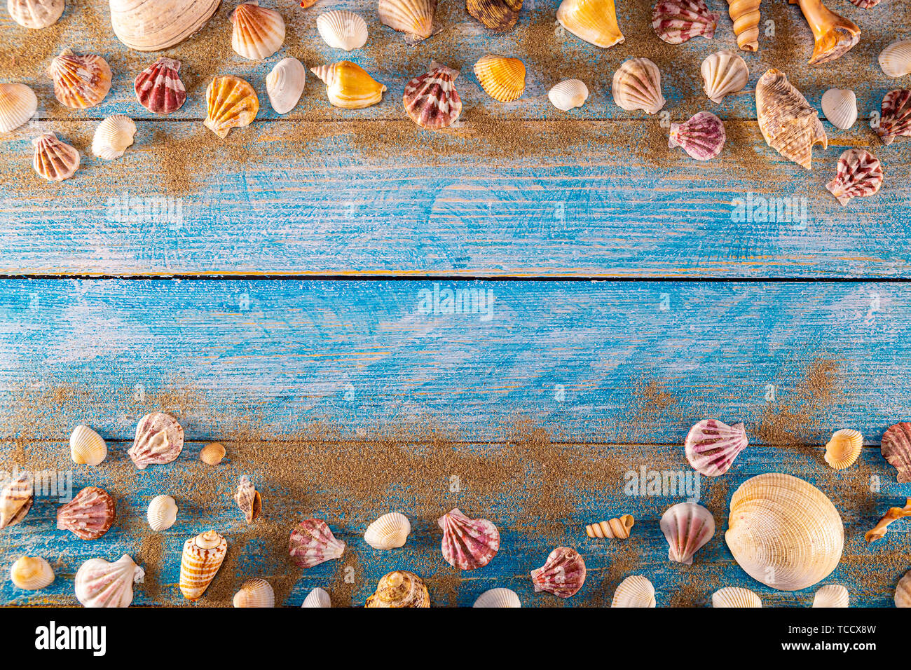 Summer time concept with sea shells on a blue wooden background and sand. Seashells frame on wooden background nautical border. Focus on seashells. Stock Photo