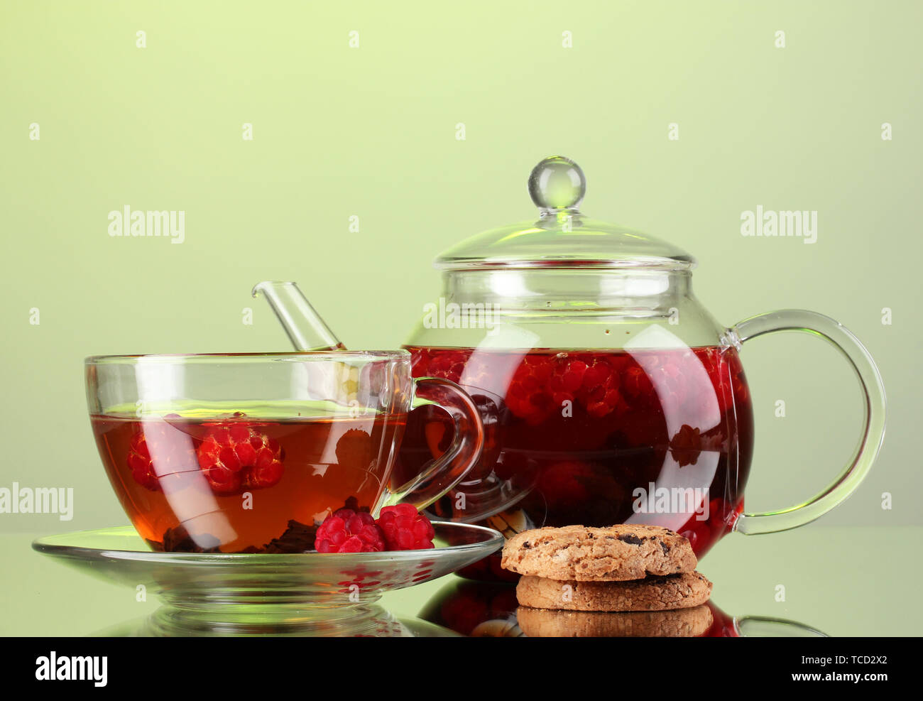 Black fruit raspberry tea in glass teapot and cup on green background ...