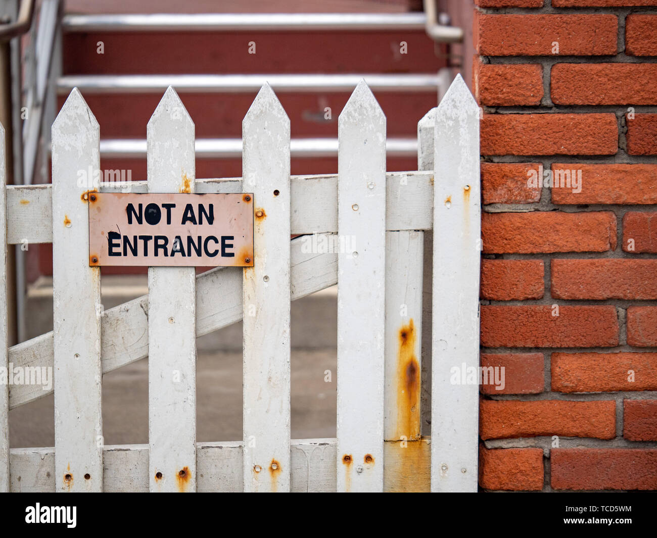 Not an entrance sign on white picket fence with rusted parts on brick building Stock Photo