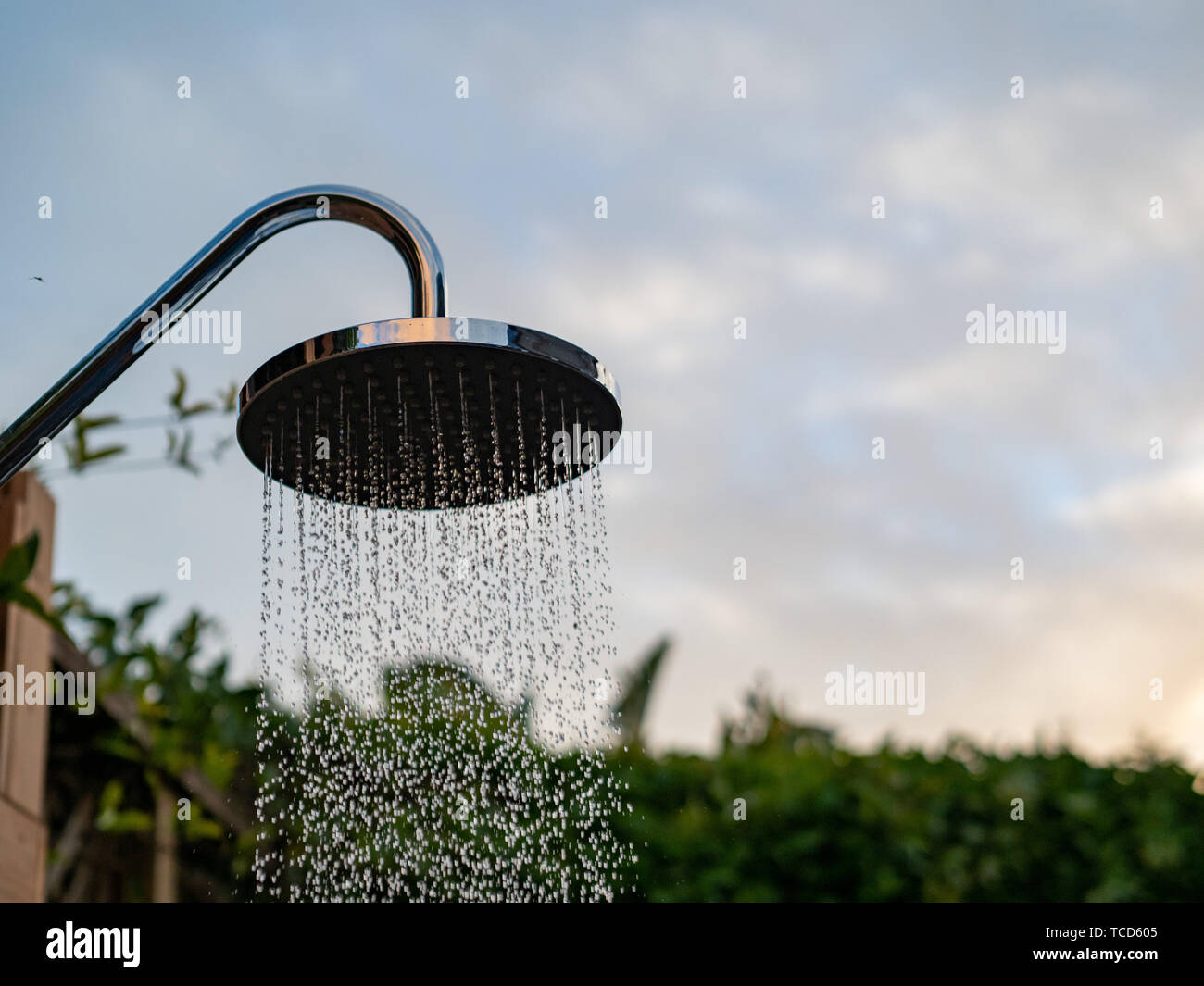 Waterfall showerhead outside in evening sky and water streaming down