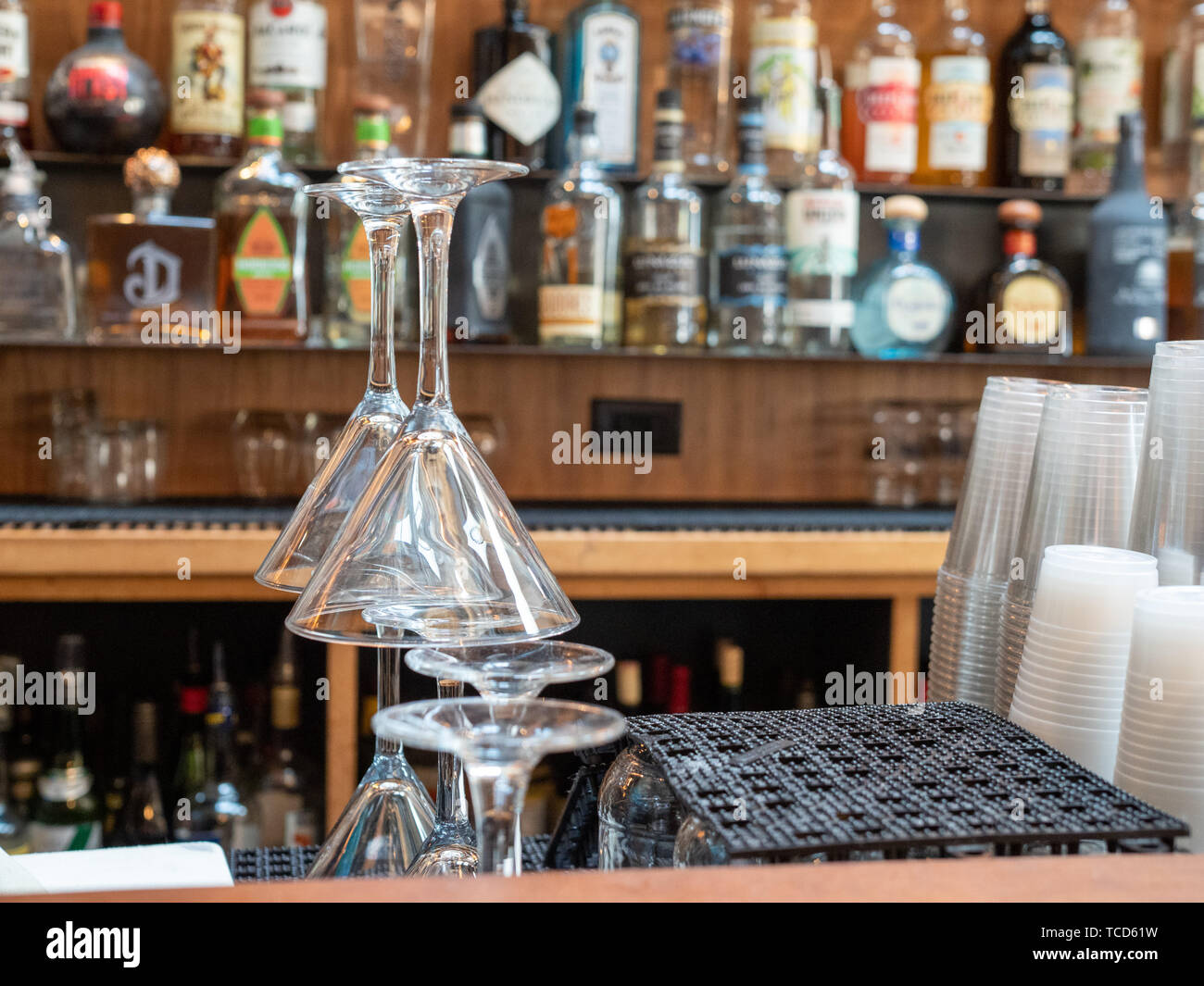 Martini glasses stacked behind a busy bar with plastic cups and liquor Stock Photo