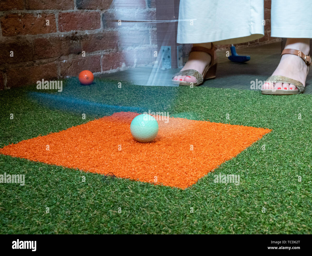 Woman playing miniature golf hitting ball with a putter mid swing Stock Photo