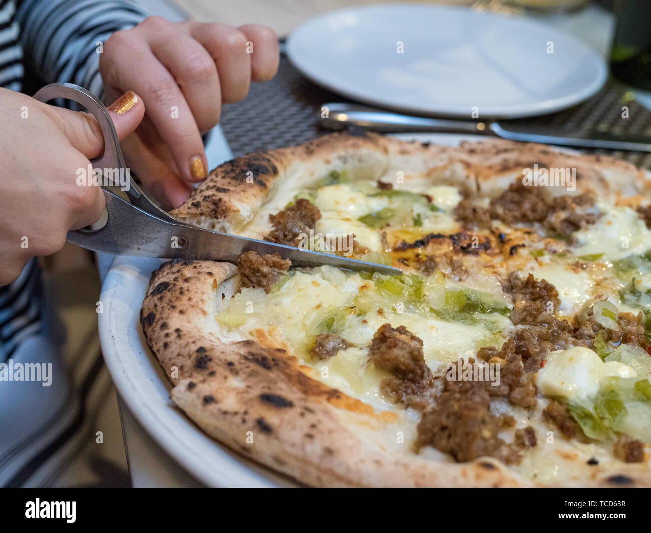 Sausage pizza being cut with traditional scissors on table being cut by
