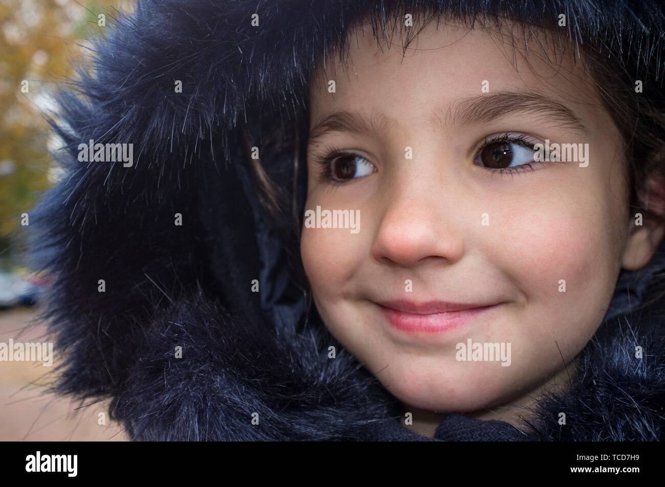 Little girl wearing dark blue winter coat with faux fur hood. Smiling