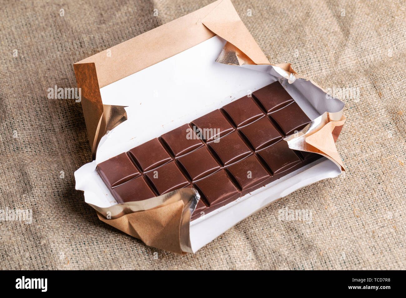Chocolate bar in paper wrapper is lying on burlap. Stock Photo