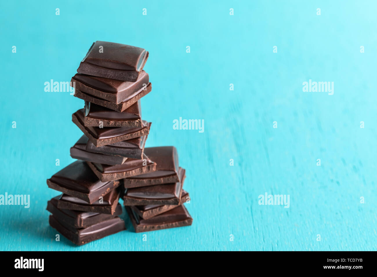 Vertical stack of squared slices of chocolate on turquoise  background. Stock Photo