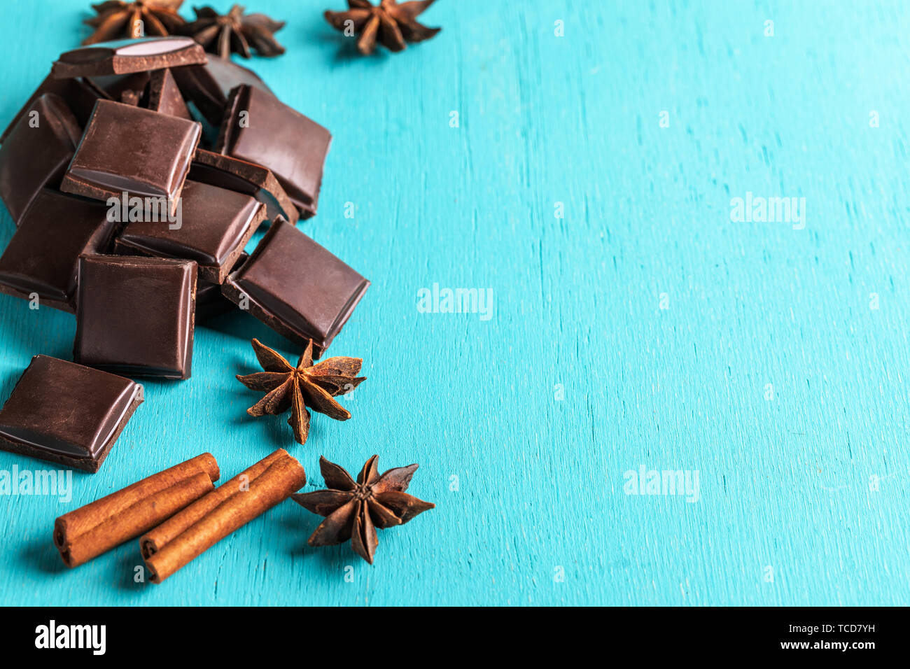 Heap of slices of chocolate, cinnamon sticks and stars anise on turquoise background. Stock Photo