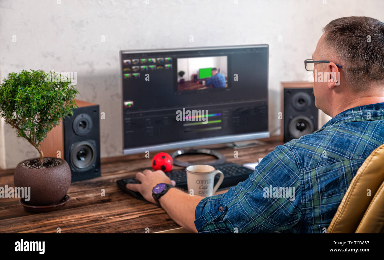 Businessman or photographer editing photographs on a large desk top monitor in an office in an over the shoulder view onto his desk Stock Photo