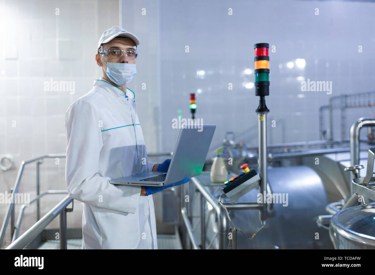 Portrait of man in a white robe and a cap standing in production department of dairy factory with laptop Stock Photo