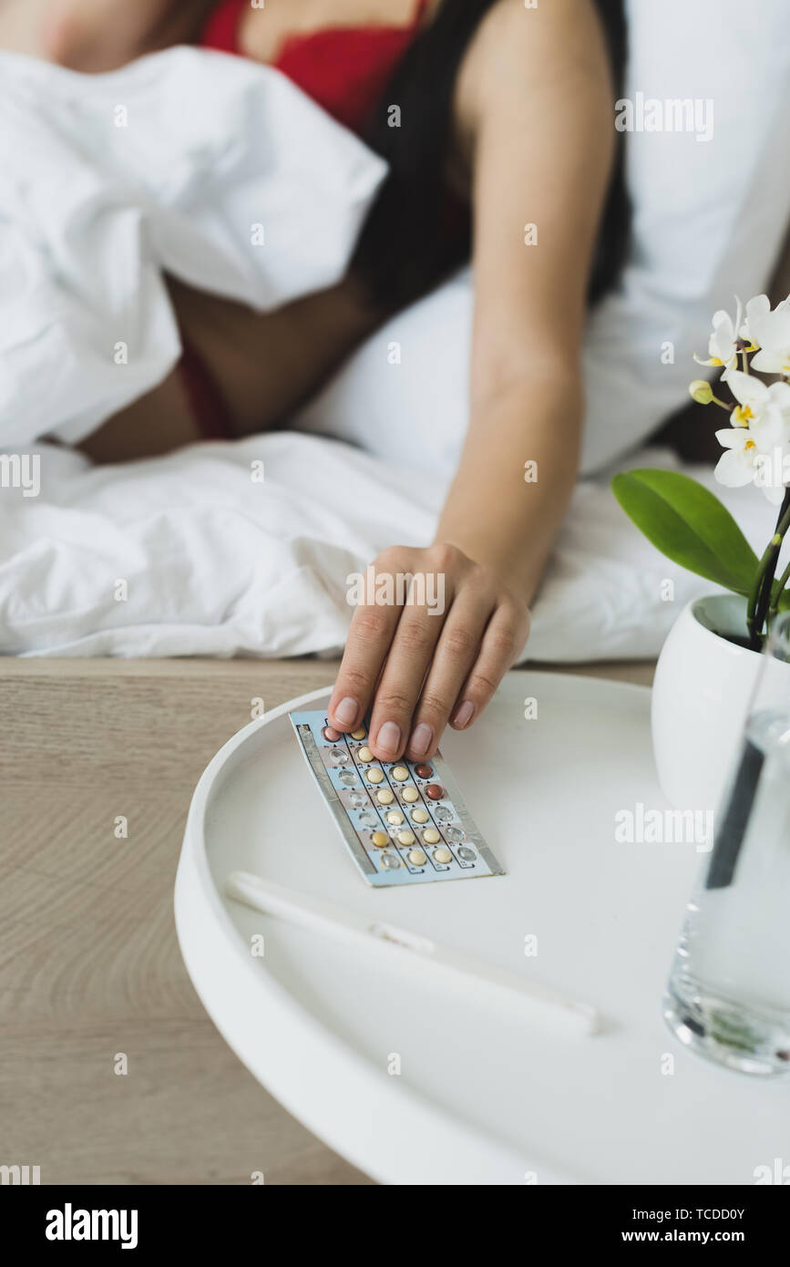 partial view of woman taking birth control pills from bedside table Stock Photo