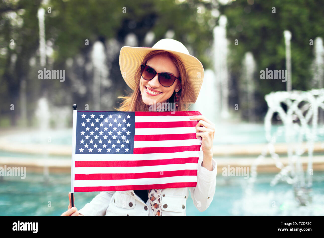 Happy young patriot urban woman in hat stretching USA flag in park, 4th of July, Indendence day Stock Photo