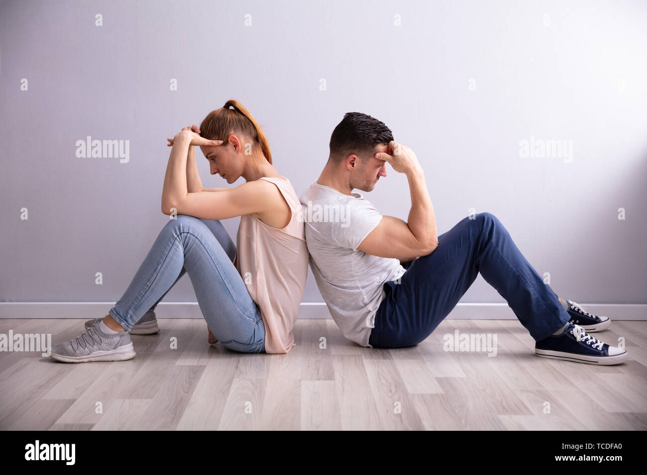 Sad Young Couple Sitting Back To Back On Floor At Home Stock Photo
