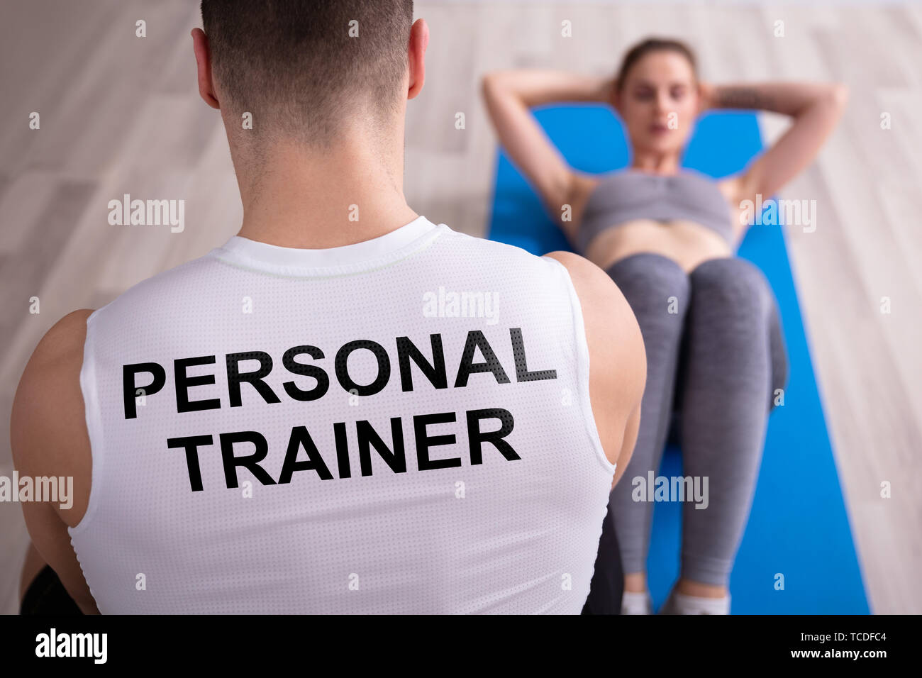 Personal Trainer Looking At Young Woman Doing Exercise On Yoga Mat Stock Photo