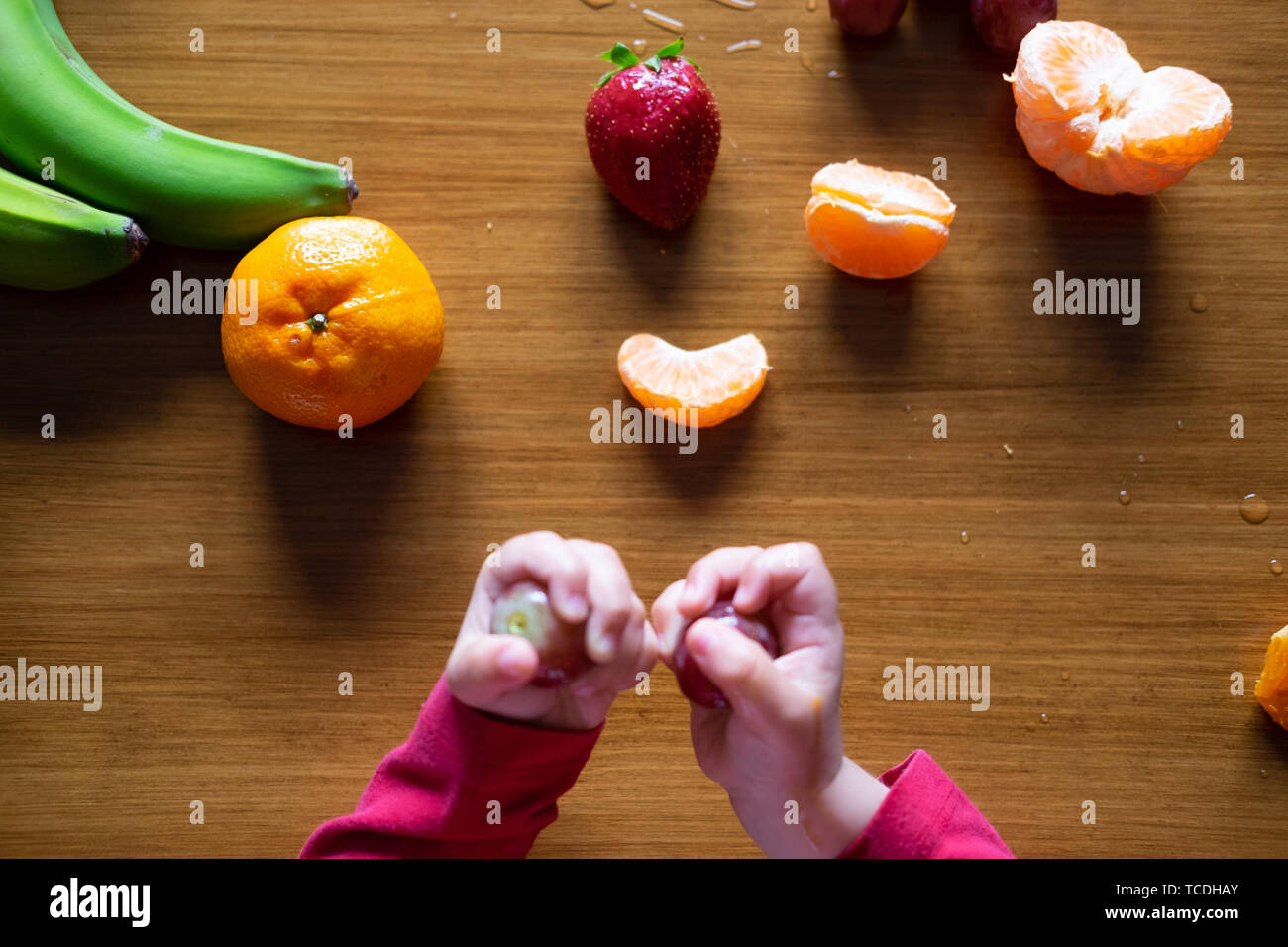 Baby s hand manipulating different fruits on a wooden table Stock Photo