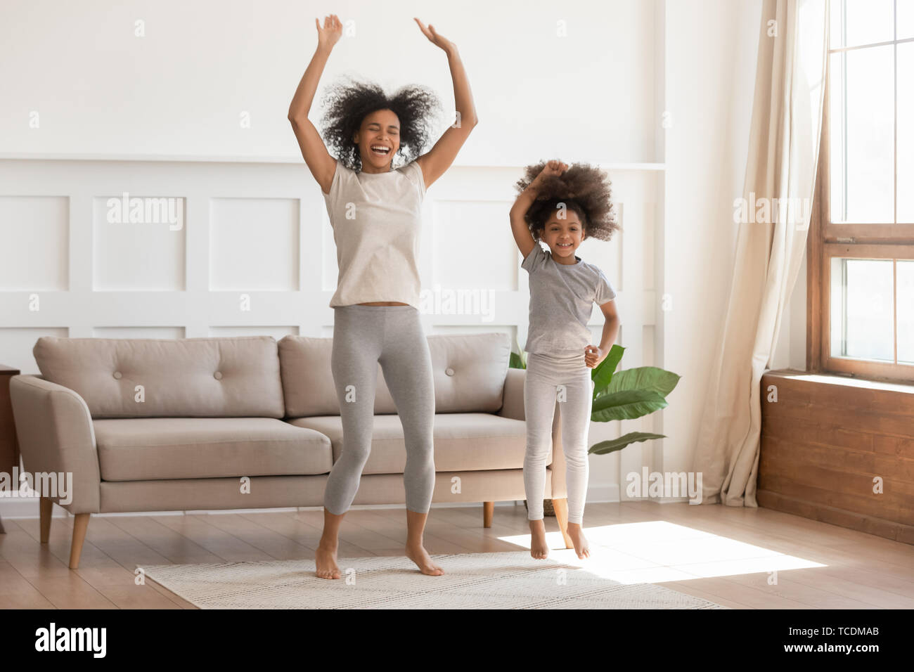 African mom with kid girl jumping dancing in living room Stock Photo